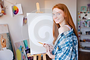 Smiling beautiful woman painter making sketches on blank canvas