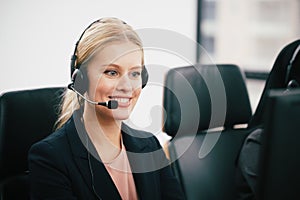 A smiling  beautiful woman sitting in a customer service department office with headset working in call center