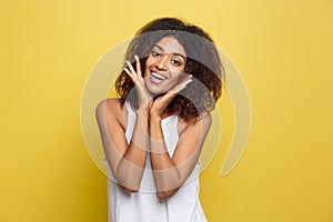 Smiling beautiful young African American woman in white T-shirt posing with hands on chin. Studio shot on Yellow