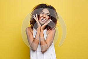 Smiling beautiful young African American woman in white T-shirt posing with hands on chin. Studio shot on Yellow