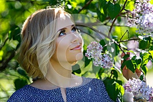 Smiling beautiful young blond girl near lilac bush