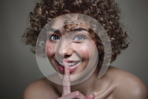 Smiling beautiful young freckled girl with keep quiet gesture, selective focus