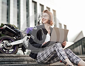 Smiling girl is sitting next to her purple motorcycle, working at the computer. photo