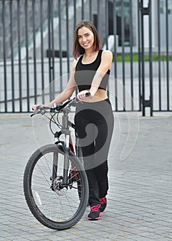 Smiling beautiful young girl standing with her bicycle on the street. City scene