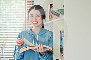 Smiling beautiful young girl standing in the library at home with books, Woman reading a book