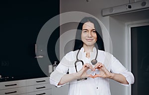 Smiling beautiful young indian ethnicity female doctor cardiologist showing heart