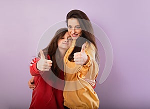 Smiling beautiful young mother and cute daughter hugging in fashion yellow and red hoodie together and showing thumb up success