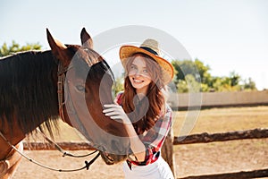 Smiling beautiful young woman cowgirl with her horse on farm