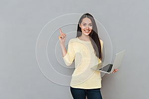 Smiling beautiful young woman holding laptop and pointing away