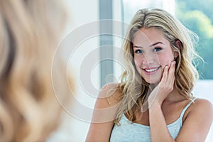 Smiling beautiful young woman looking at herself in the bathroom mirror