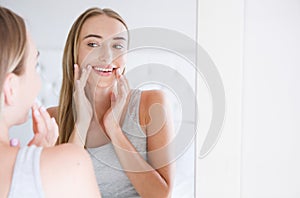 Smiling beautiful young woman looking into a mirror at herself in room. Beauty, hygiene, morning and people concept