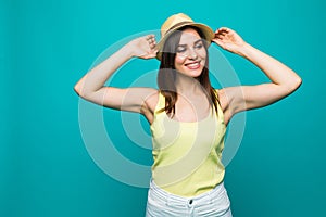 Smiling beautiful young woman posing with hands on hat on turquoise background. photo