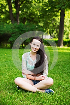Smiling beautiful young woman sitting on grass.