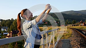 Smiling beautiful young woman taking pictures with smartphone in mountains