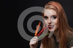 Smiling beautiful young woman is tasting red chili pepper