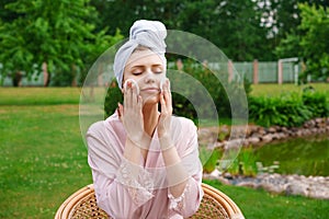 Smiling beautiful young woman with towel on head hold cotton pad cleansing face