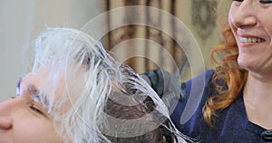 Smiling beauty salon worker in black gloves applies bleach