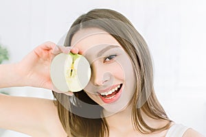 Smiling beauty woman holding half of green apple. The girl closes one eye with half an apple.