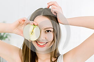 Smiling beauty woman holding half of green apple. The girl closes one eye with half an apple.