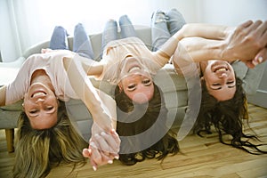 smiling best girl friends blond and brunette lay upside down on sofa