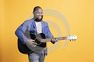 Smiling BIPOC singer holding guitar, performing blues tunes, studio background