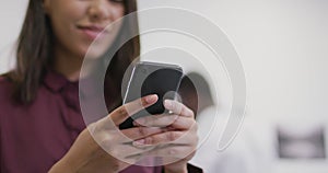 Smiling biracial businesswoman using smartphone with colleagues in background in modern office