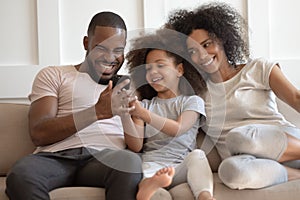 Smiling biracial family with kid laugh enjoy video on cell