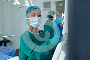 Smiling biracial female surgeon operating computerised medical equipment in operating theatre