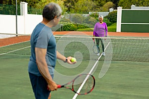 Smiling biracial senior woman playing tennis with senior husband at tennis court