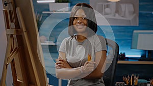 Smiling black artist sitting in art studio space with craft tools