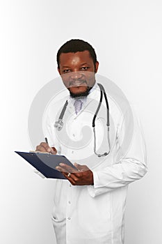Smiling black bearded doctor man in white robe with stethoscope filling medical records on clipboard