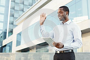 Smiling black businessman with tablet smiling and making welcoming gesture