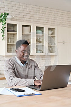 Smiling black businessman working remotely from homeoffice on laptop computer.