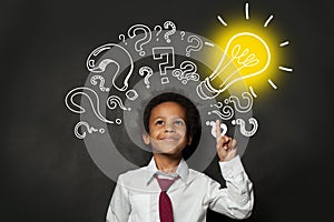 Smiling black child student with lightbulb on blackboard background. Brainstorming and idea concept photo