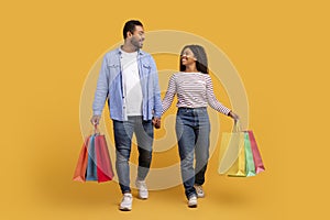 Smiling black couple carrying bright shopping bags, walking and holding hands