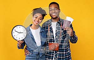 Smiling Black Couple Holding Tickets And Clock Over Yellow Background