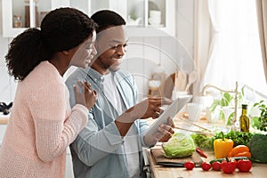 Smiling Black Couple Using Digital Tablet While Cooking In Kitchen, Searching Recipe