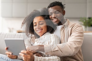 Smiling black couple websurfing social media on tablet gadget indoor