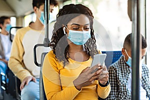 Beautiful smiling black woman in mask listening music in bus