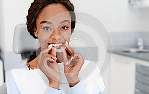 Smiling black girl holding invisible aligner, modern teeth trainer