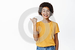 Smiling black girl pointing left, proudly showing advertisement, store sale or company brand name on empty space