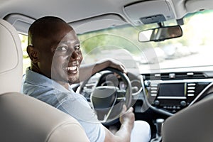 Smiling black guy driver sitting inside brand new car