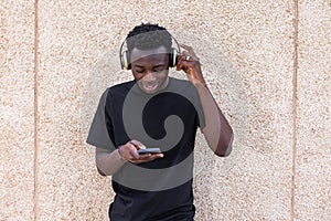 Smiling black guy using smartphone and listening to music in headphones