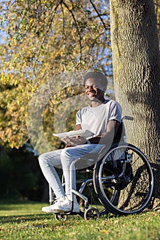 Smiling Black guy in wheelchair enjoying lunch in city park