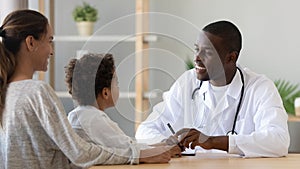 Smiling black male doctor listening to little patient make notes