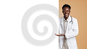 Smiling black male doctor pointing at big blank advertisement board with palm