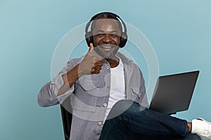 Smiling black man with headphones using laptop showing thumb