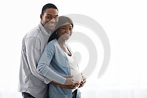 Smiling black man hugging his pregnant woman over white background