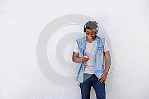 Smiling black man leaning against wall with smart phone and headphones