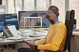 Smiling black man looking at camera at workplace in software development